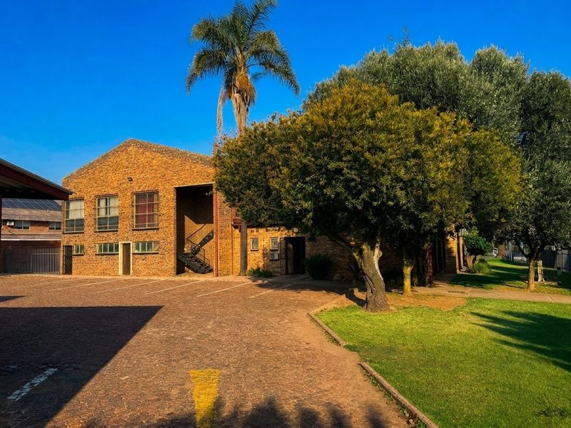 Front view of a commercial property featuring an exposed brick facade, paved driveway, and established garden area.