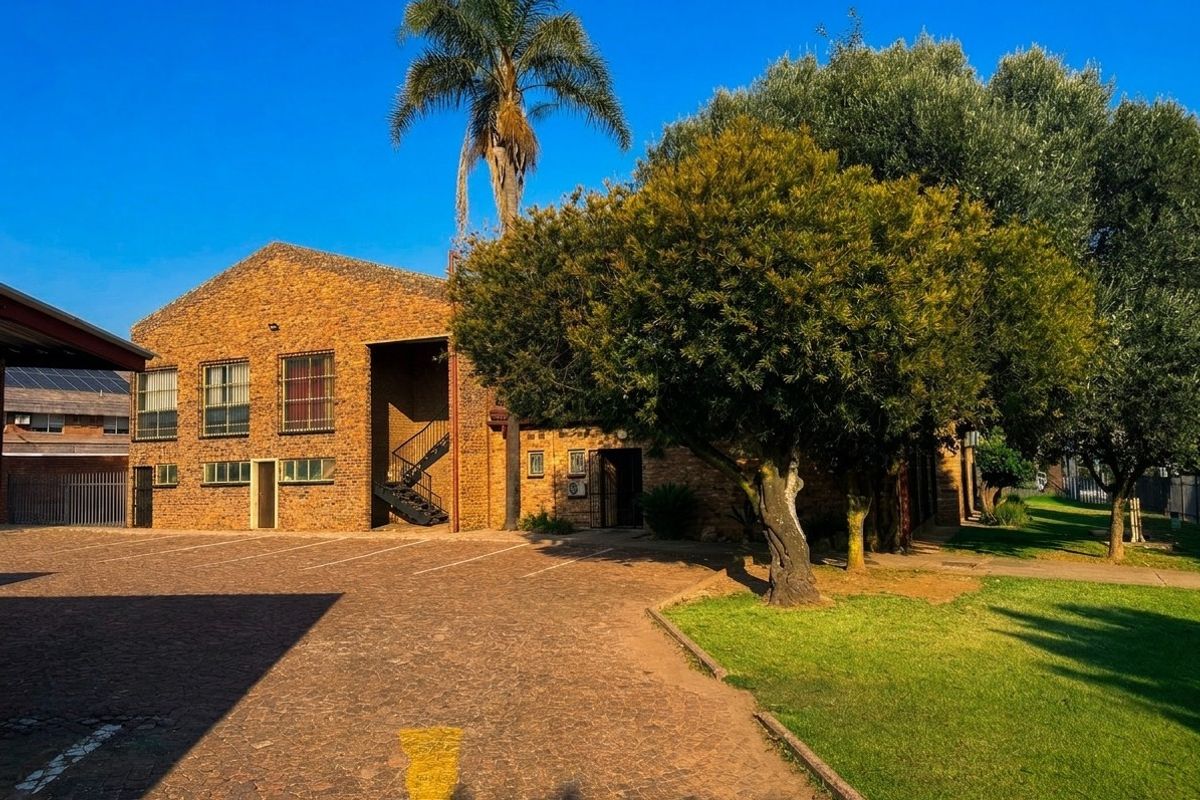 Front view of a commercial property featuring an exposed brick facade, paved driveway, and established garden area.