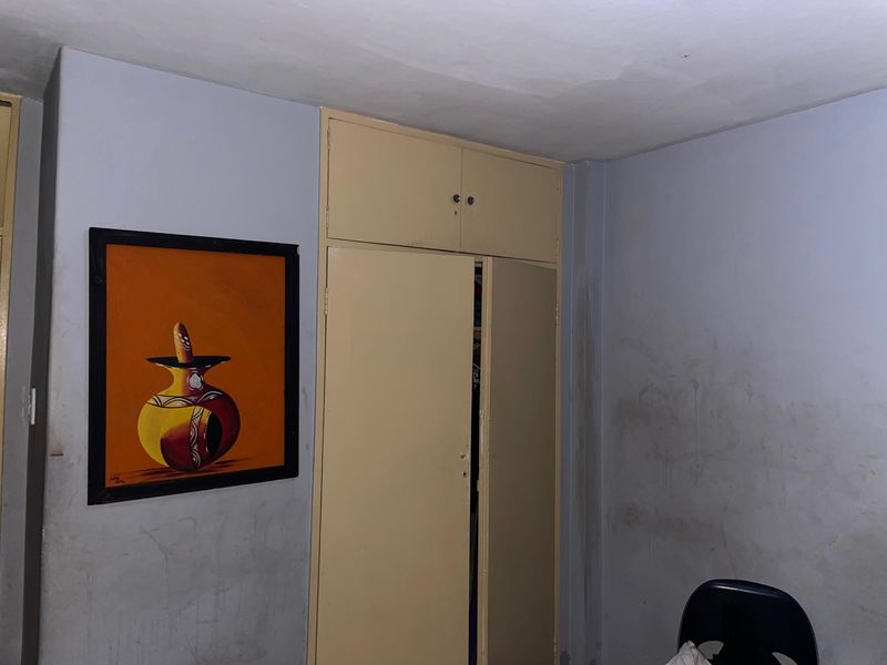 A bedroom interior featuring a built-in cupboard with overhead storage, showing signs of wear on the surrounding wall surfaces.