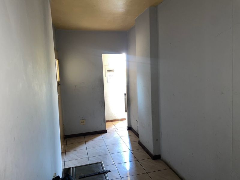 A vacant hallway featuring tiled flooring and neutral wall finishes, leading towards an adjacent room with natural light.