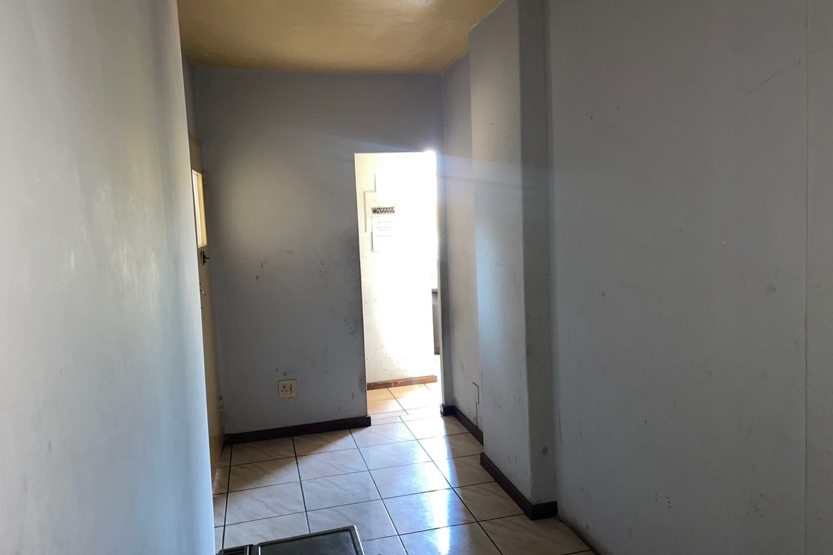 A vacant hallway featuring tiled flooring and neutral wall finishes, leading towards an adjacent room with natural light.