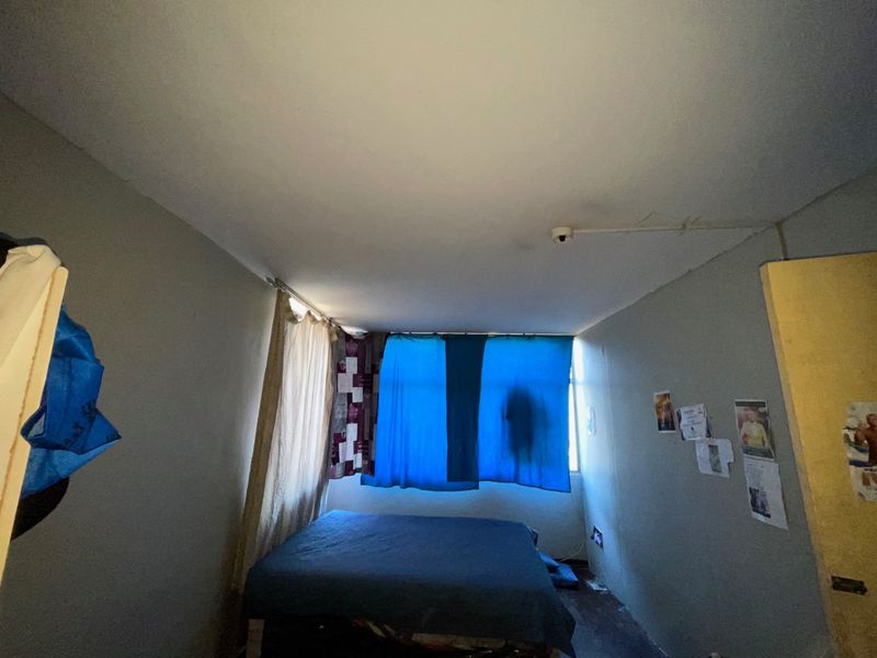 A bedroom featuring a ceiling-mounted smoke detector, requiring cosmetic updates to the walls and flooring to improve the overall condition.