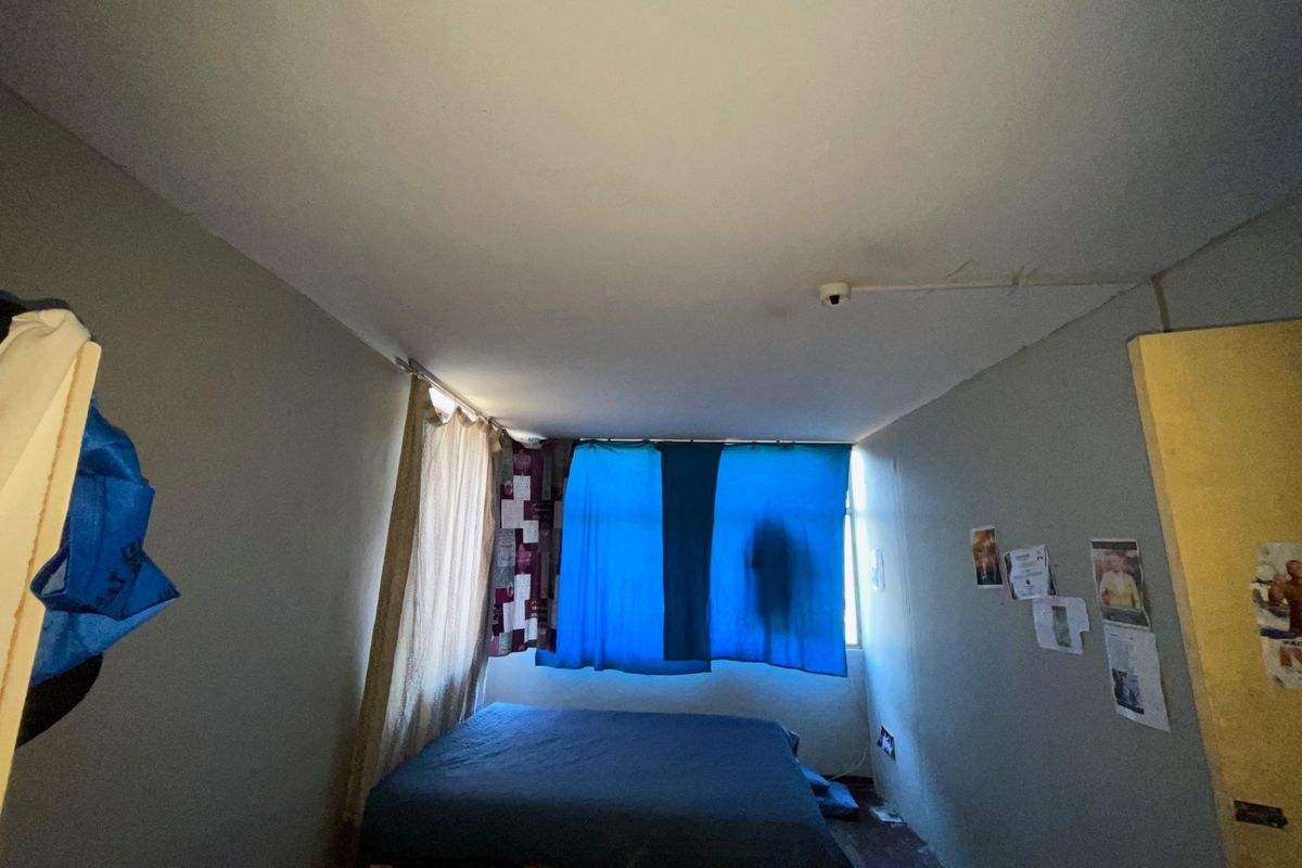 A bedroom featuring a ceiling-mounted smoke detector, requiring cosmetic updates to the walls and flooring to improve the overall condition.