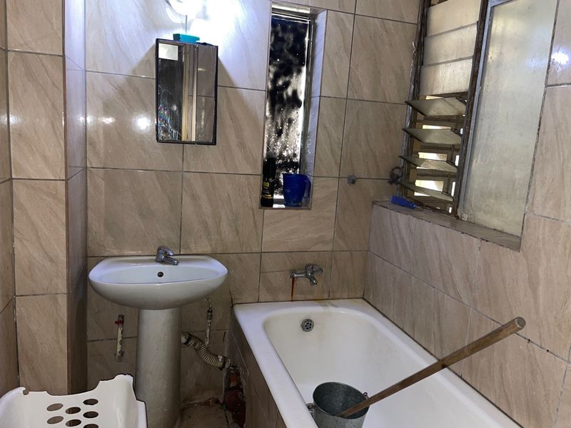 A dated bathroom featuring a pedestal basin, bathtub, and tiled walls, currently requiring significant renovation and modernization of fixtures and finishes.