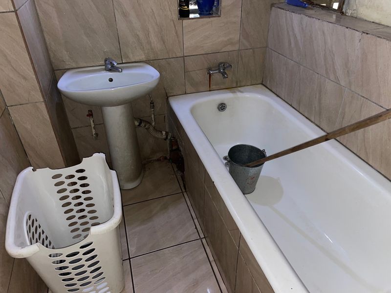 A compact bathroom featuring a pedestal basin and bathtub with neutral wall and floor tiling, currently requiring maintenance and cosmetic updates.