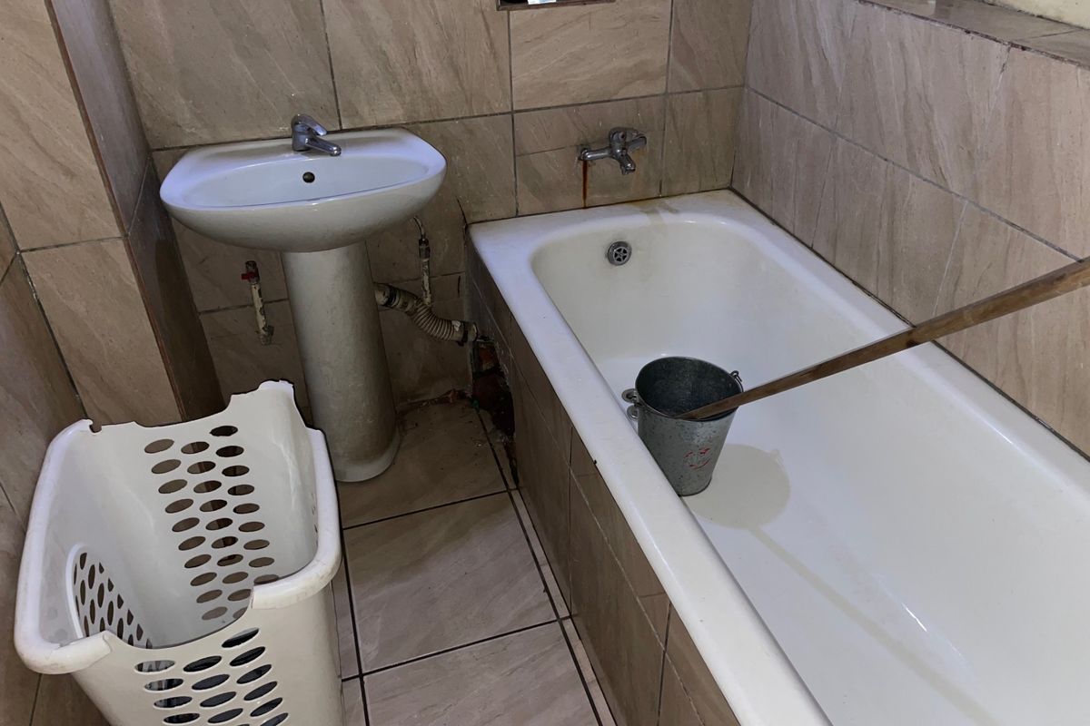 A compact bathroom featuring a pedestal basin and bathtub with neutral wall and floor tiling, currently requiring maintenance and cosmetic updates.