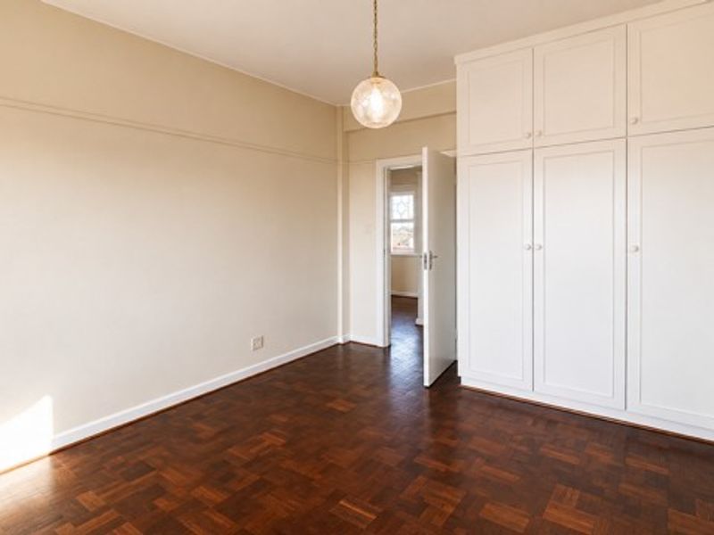 A bright, empty bedroom featuring classic parquet flooring, built-in floor-to-ceiling cupboards, and a decorative picture rail.