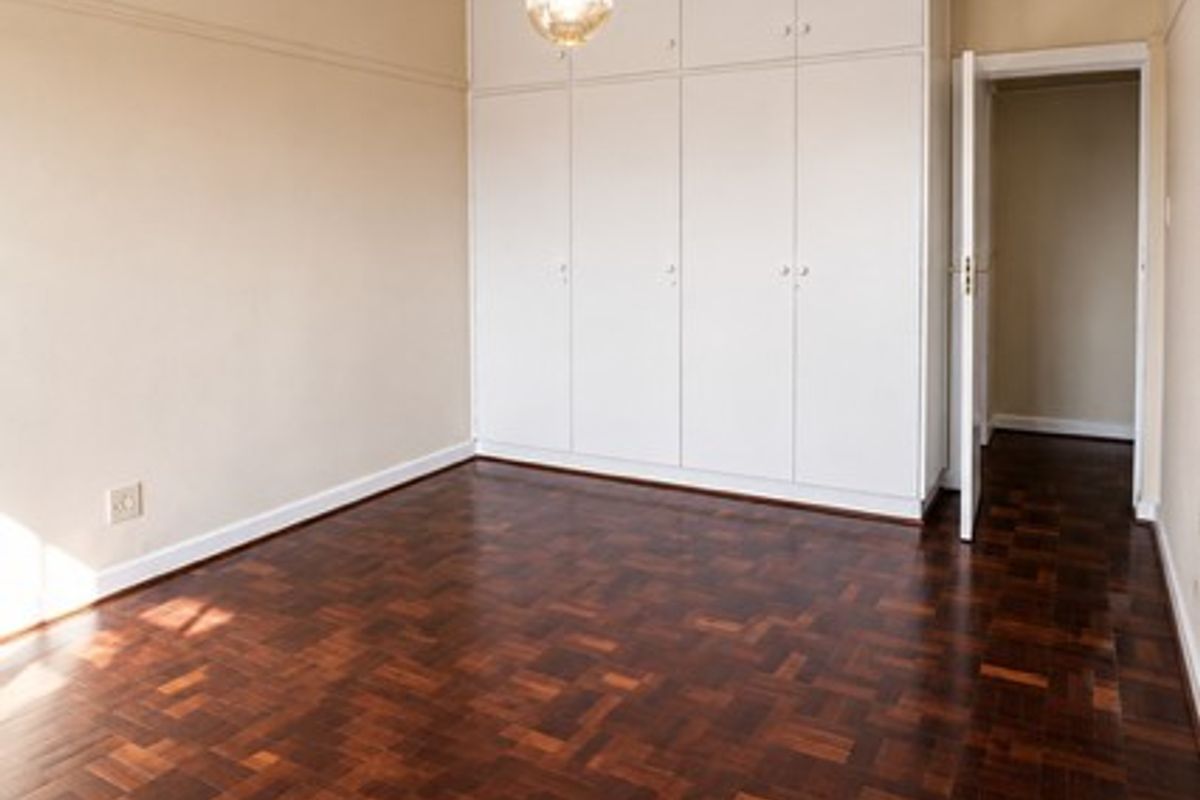 A spacious, empty bedroom featuring classic dark parquet flooring, ample built-in storage cupboards, and a central pendant light fixture.