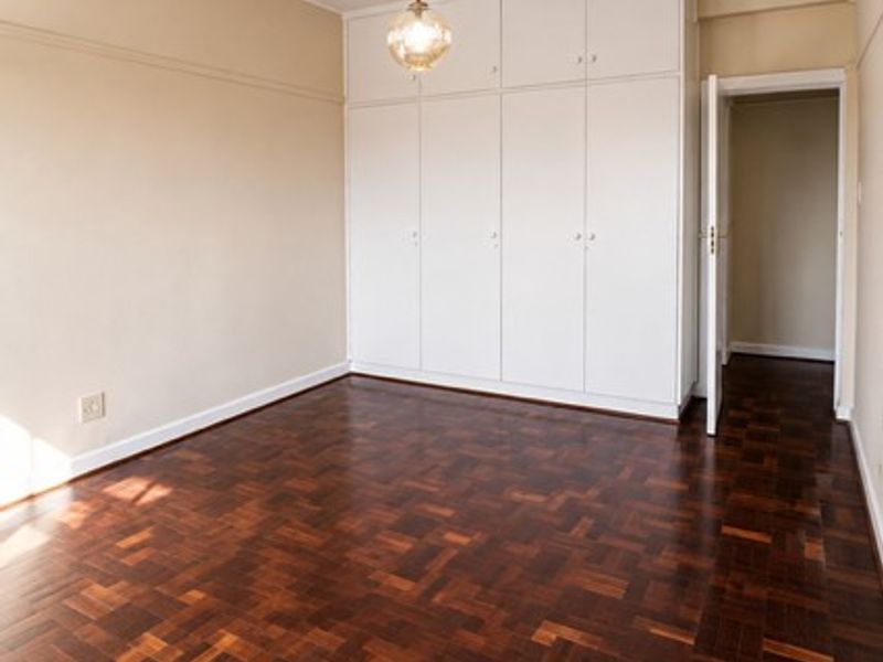 A spacious, empty bedroom featuring classic dark parquet flooring, ample built-in storage cupboards, and a central pendant light fixture.