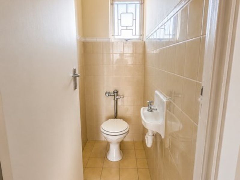 A compact guest bathroom featuring a wall-mounted toilet, a small wall-mounted basin, and neutral ceramic tiling throughout.