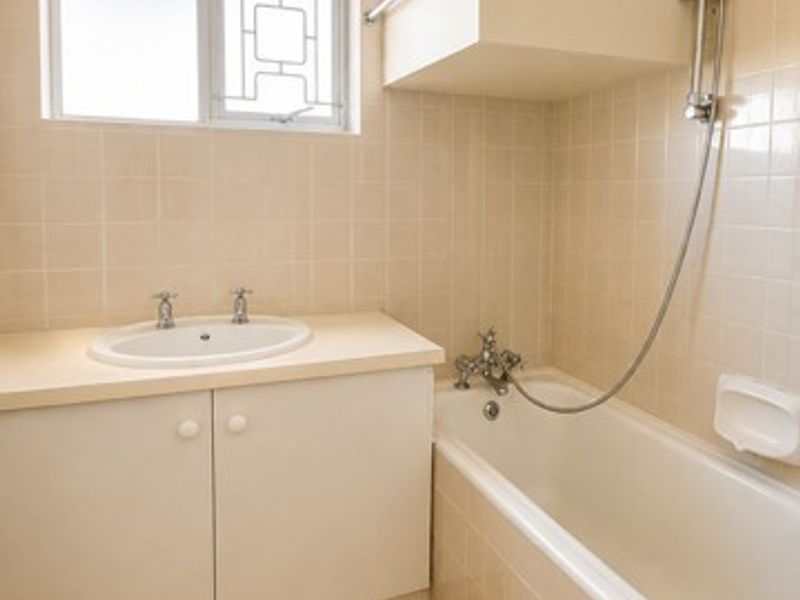 A functional bathroom featuring a built-in vanity, bathtub with shower mixer, and neutral tiled finishes throughout.
