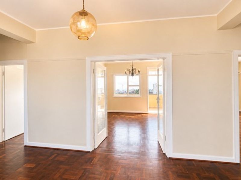 Spacious living area featuring original parquet flooring, classic picture rails, and double glass-panel doors leading to an adjoining room.