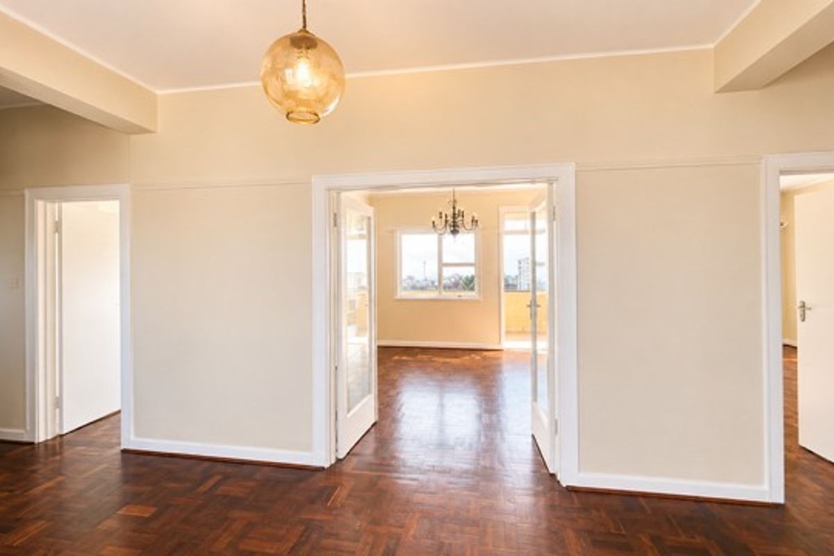 Spacious living area featuring original parquet flooring, classic picture rails, and double glass-panel doors leading to an adjoining room.