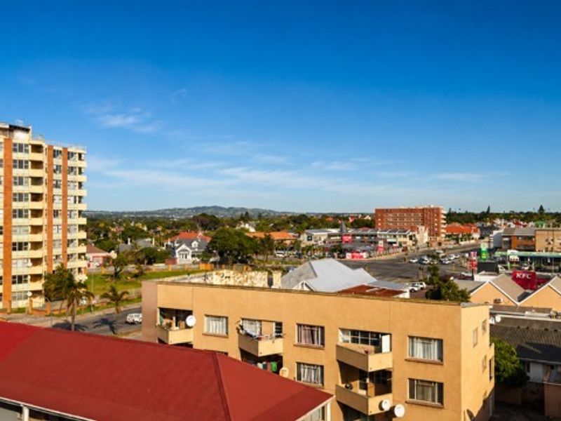 An elevated urban view overlooking surrounding apartment buildings, commercial areas, and distant hills under a clear blue sky.