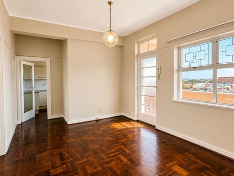 A bright, empty living room featuring classic parquet flooring, a decorative leaded glass window, and access to an outdoor area.