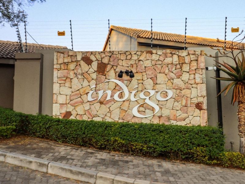 The entrance to the Indigo complex featuring a stone-clad signage wall, electric security fencing, and manicured landscaping.