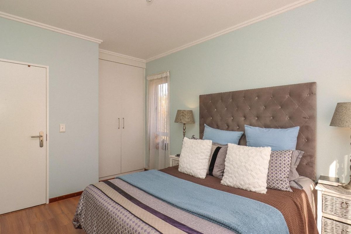 A well-maintained bedroom featuring laminate flooring, built-in wardrobe storage, and neutral wall finishes.