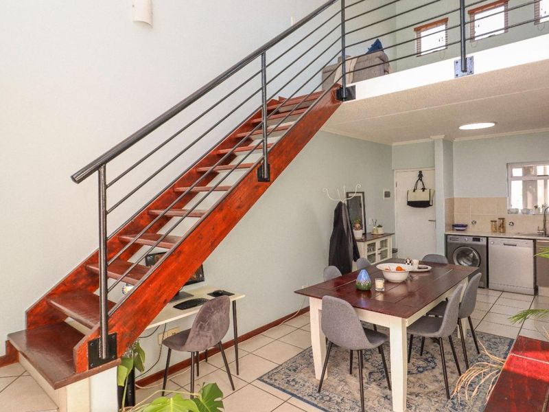 Open-plan living area featuring a wooden staircase with metal balustrade, tiled flooring, and a functional kitchen space with integrated laundry connections.