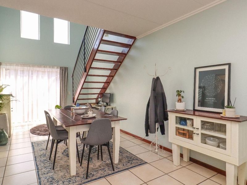 Open-plan living and dining area featuring tiled flooring, a wooden staircase, and high ceilings with natural light from a sliding glass door.