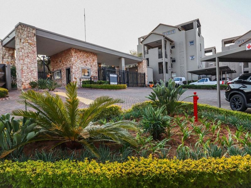 The entrance to the apartment complex features a secure gatehouse with stone cladding, paved driveway, and well-maintained landscaped gardens with covered parking bays.
