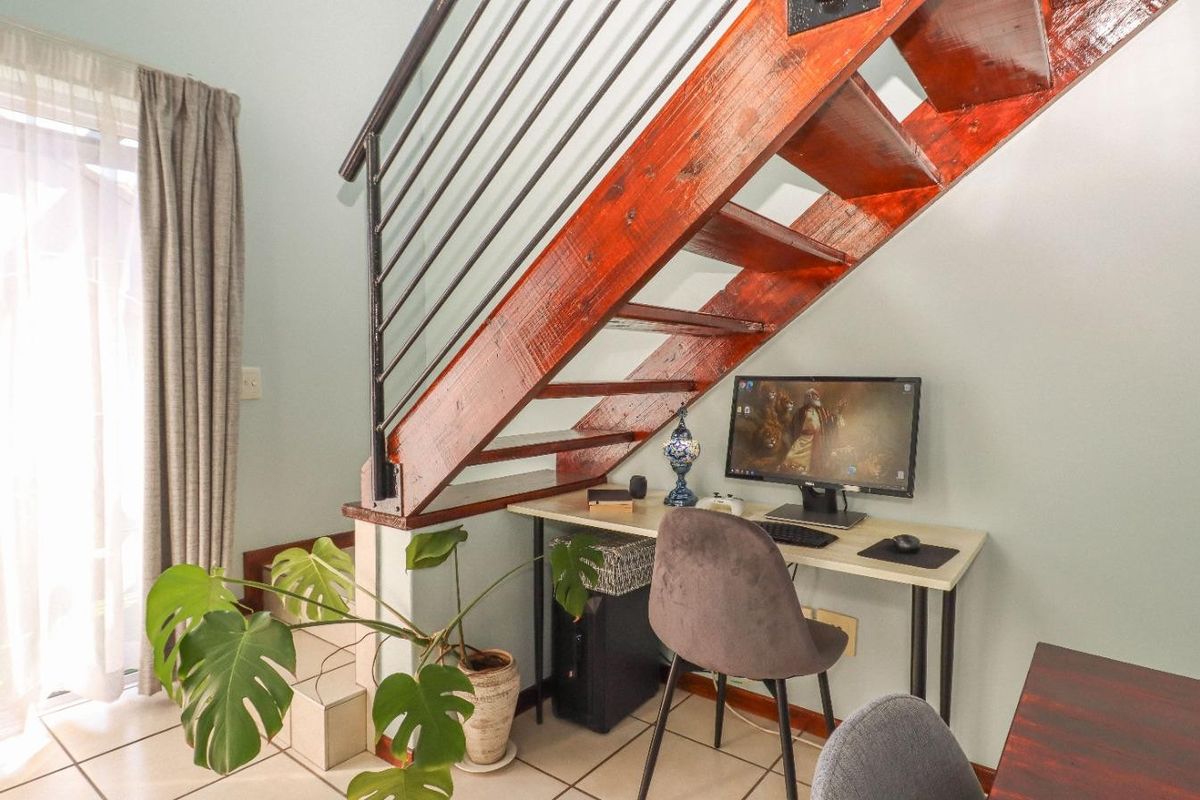 A living area featuring a wooden staircase with a metal balustrade, tiled flooring, and a sliding glass door providing natural light.