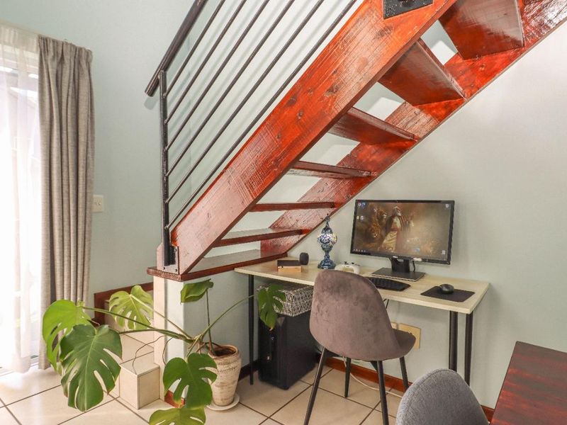 A living area featuring a wooden staircase with a metal balustrade, tiled flooring, and a sliding glass door providing natural light.