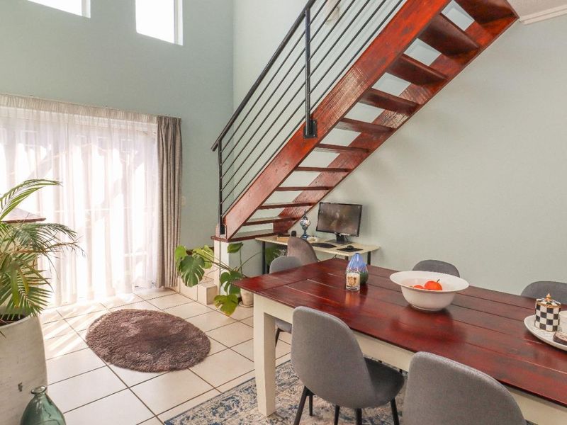 Open plan living area featuring high ceilings, tiled flooring, and a wooden staircase with a metal balustrade leading to the upper level.