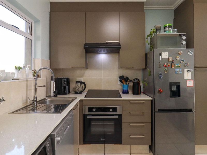A compact, well-maintained kitchen featuring modern taupe cabinetry, stone countertops, a built-in oven with hob, and a tiled backsplash.