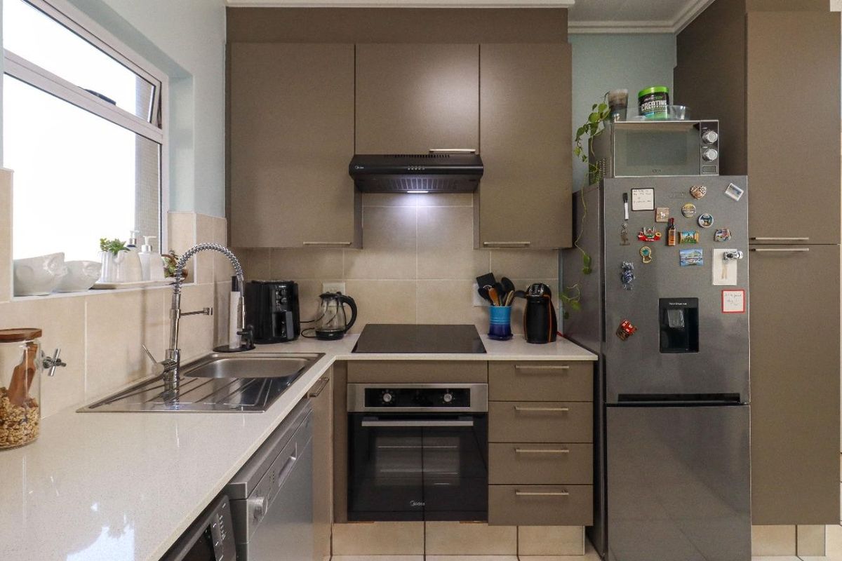 A compact, well-maintained kitchen featuring modern taupe cabinetry, stone countertops, a built-in oven with hob, and a tiled backsplash.