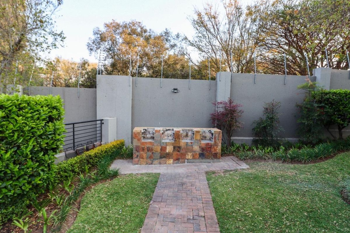 A private rear garden featuring a built-in stone-clad braai, brick paved walkway, and secure perimeter wall with electric fencing.