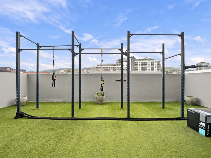 Outdoor gym area featuring a professional-grade fitness rig installed on artificial turf with perimeter wall enclosure.