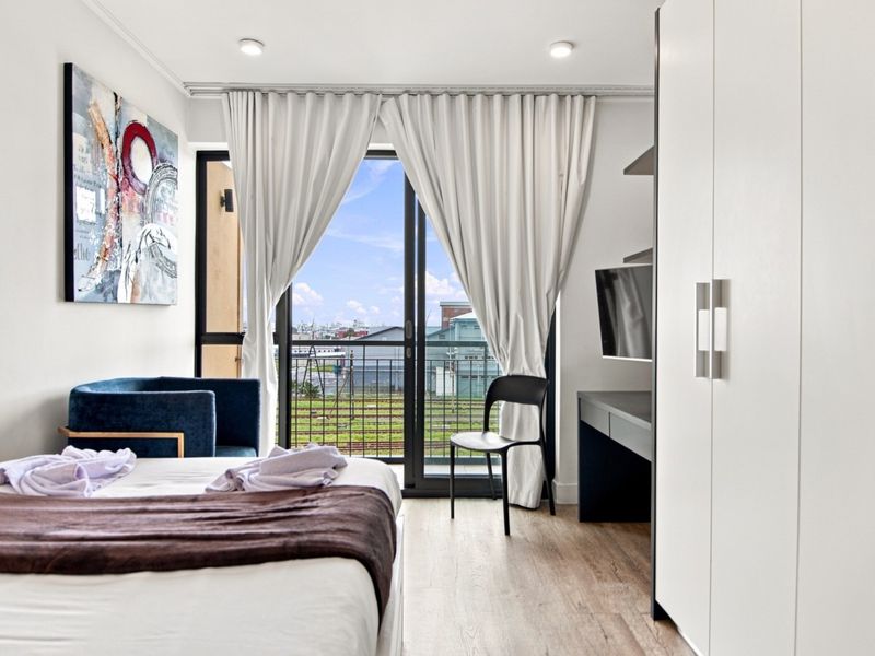 Modern bedroom featuring laminate flooring, built-in wardrobe, and a sliding glass door providing access to a private balcony with an urban view.