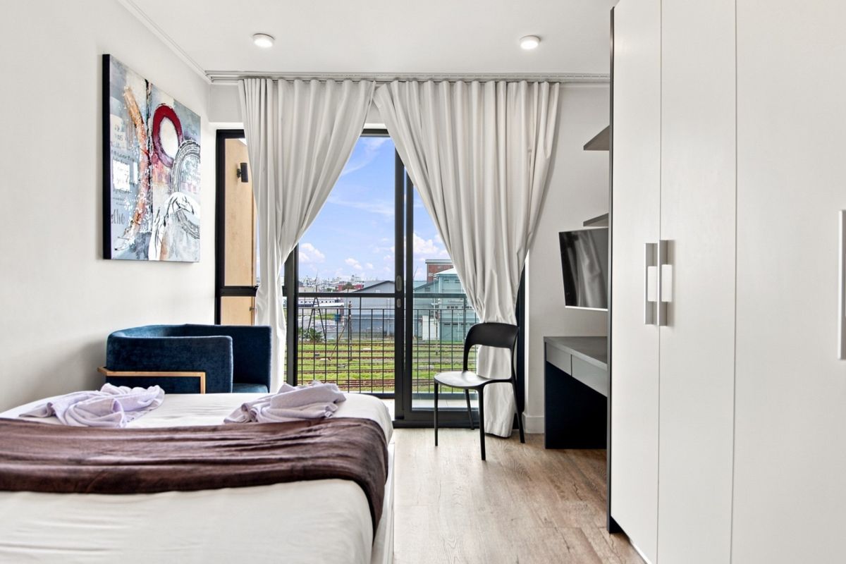 Modern bedroom featuring laminate flooring, built-in wardrobe, and a sliding glass door providing access to a private balcony with an urban view.