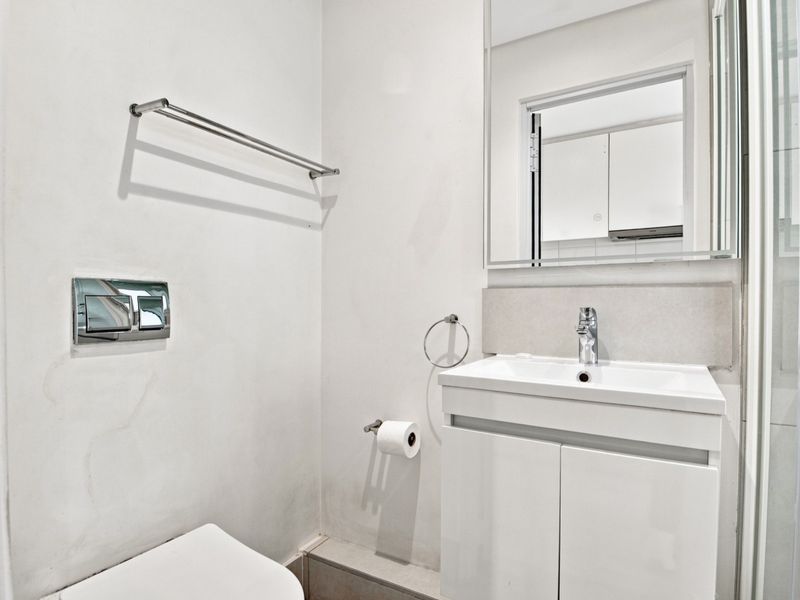 A clean, modern bathroom featuring a wall-mounted toilet, vanity cabinet with basin, and a shower enclosure.