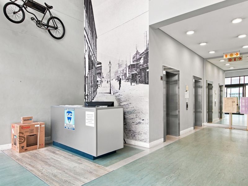 Modern apartment building entrance lobby featuring a reception desk, multiple elevators, and clean, well-maintained finishes.