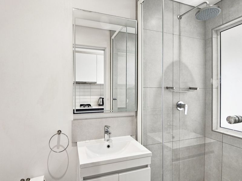 Modern bathroom featuring a vanity with basin, wall-mounted mirror, and a glass-enclosed shower with a rain shower head and grey wall tiling.