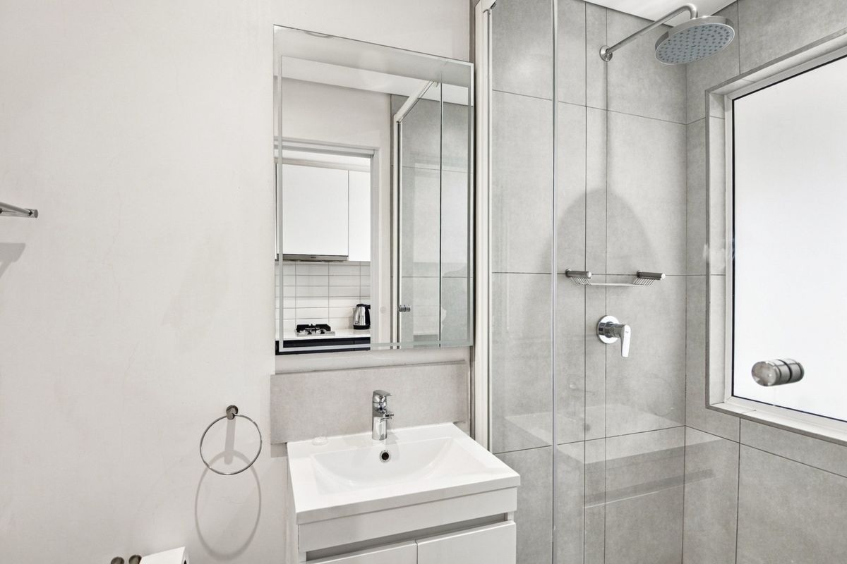 Modern bathroom featuring a vanity with basin, wall-mounted mirror, and a glass-enclosed shower with a rain shower head and grey wall tiling.