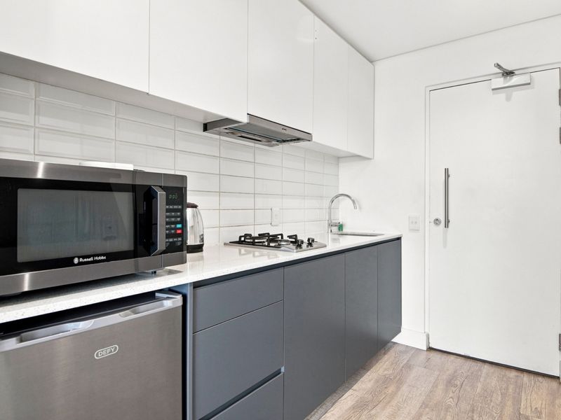 Modern compact kitchen featuring sleek two-tone cabinetry, stone countertops, gas hob, extractor fan, and a stylish subway tile backsplash.