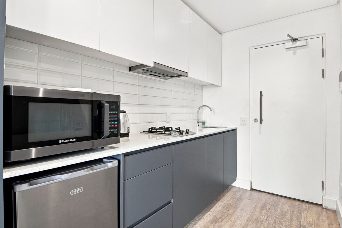Modern compact kitchen featuring sleek two-tone cabinetry, stone countertops, gas hob, extractor fan, and a stylish subway tile backsplash.