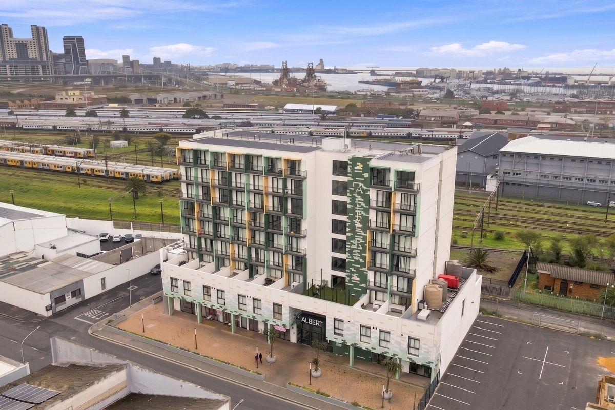 Aerial view of The Albert apartment building, showcasing its modern facade, balconies, and surrounding urban infrastructure near the harbor and railway lines.