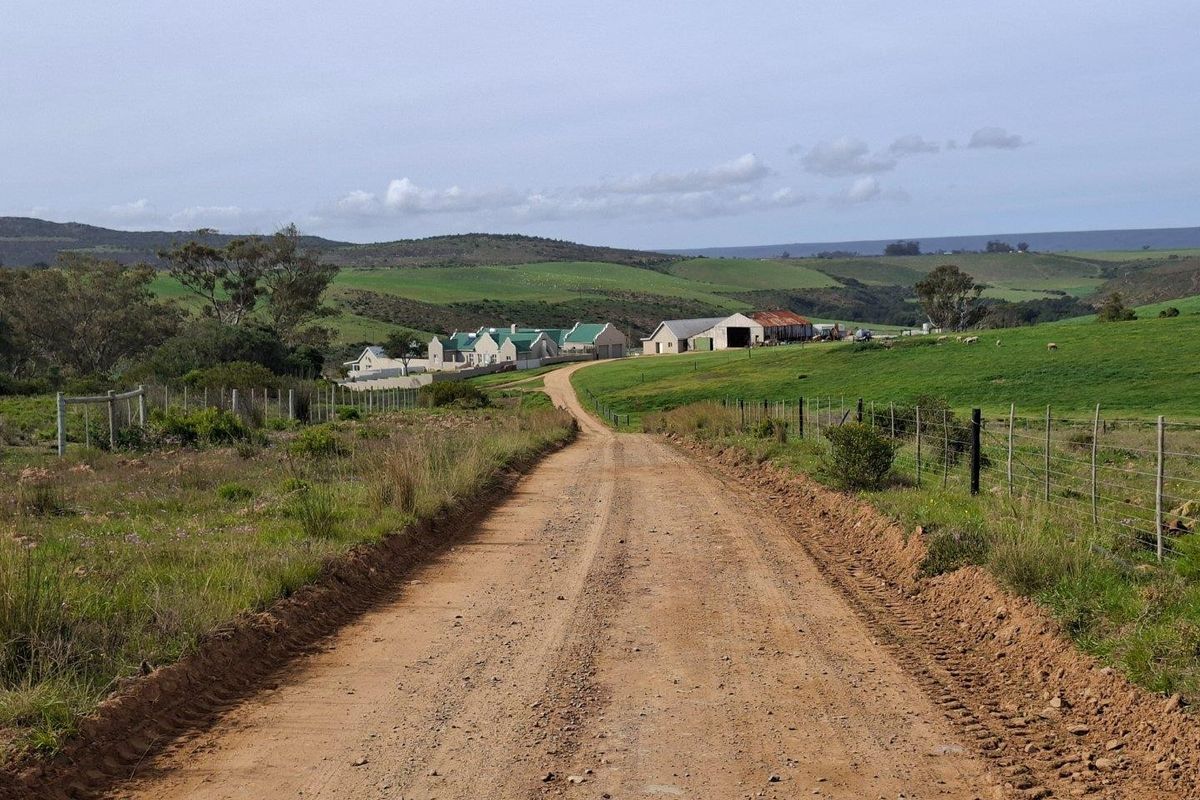A scenic view of a dirt access road leading towards a collection of farm buildings set within rolling green hills.