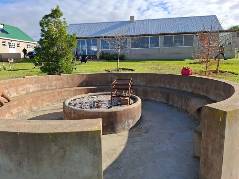 Outdoor garden area featuring a circular built-in concrete fire pit with integrated bench seating, set against the backdrop of a farm-style building.