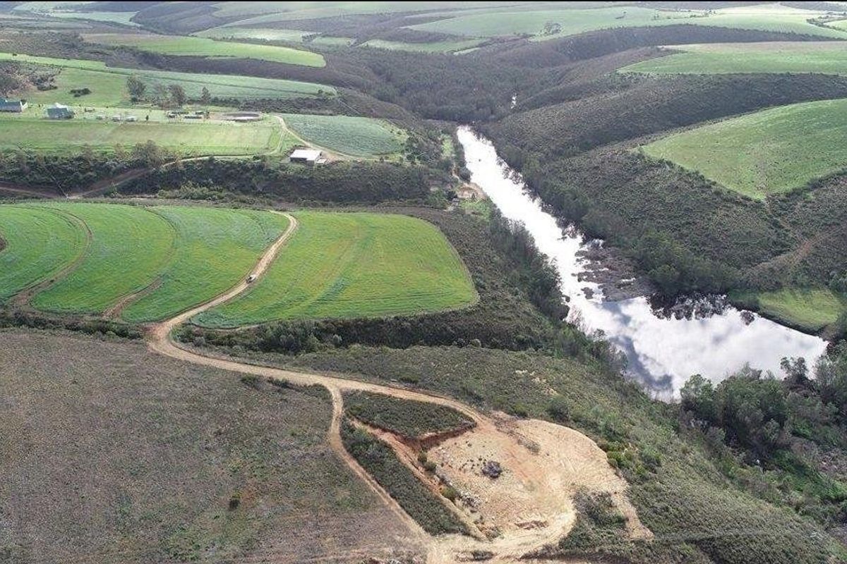 Aerial view of expansive farm landscape featuring rolling green fields, a natural river, and established dirt access roads.