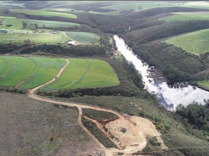 Aerial view of expansive farm landscape featuring rolling green fields, a natural river, and established dirt access roads.
