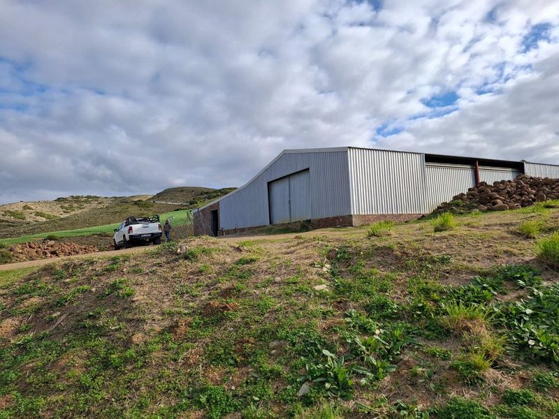 A large agricultural shed with corrugated metal siding and a sliding door, situated on a rural farm property.