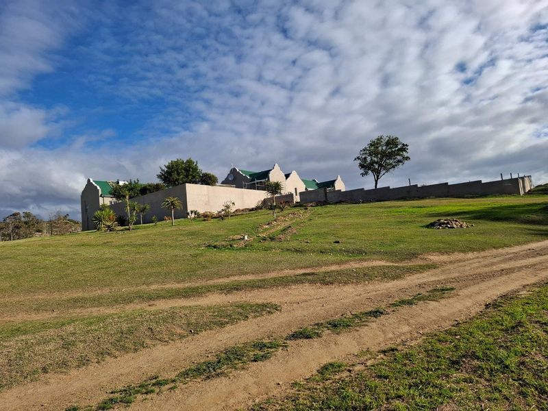 A view of the farm property featuring a gabled building with a metal roof, enclosed by a perimeter wall on a large grassy plot.
