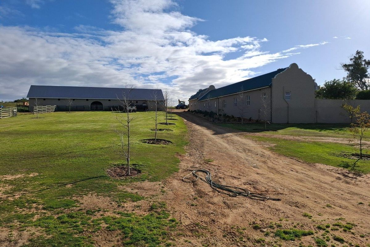 A view of the farm property featuring large outbuildings with metal roofing, a dirt driveway, and expansive lawn areas.