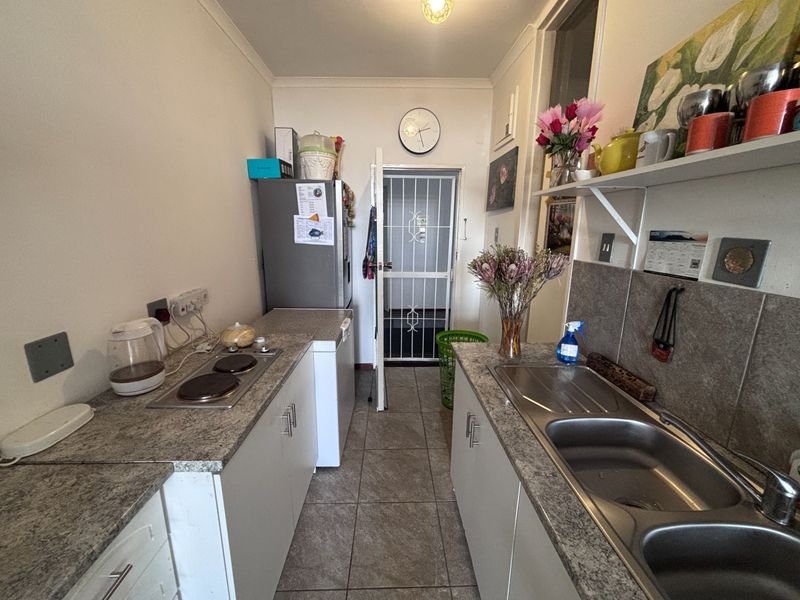 Compact galley-style kitchen featuring laminate countertops, a stainless steel double sink, built-in electric hob, and tiled flooring with direct access to a security gate.