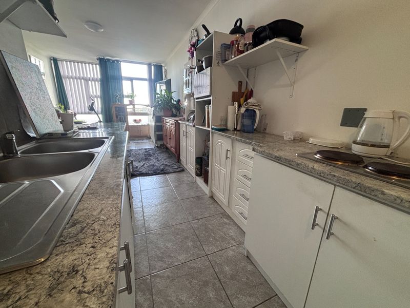 A functional galley-style kitchen featuring laminate countertops, built-in cabinetry, and a double bowl stainless steel sink, with direct access to the living area.