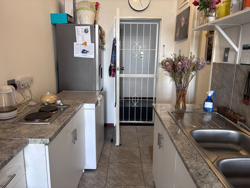 Compact kitchen featuring laminate countertops, a stainless steel double sink, electric hob, and tiled flooring, with a secure entrance gate.